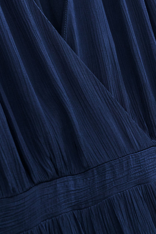 ba&sh Natalia Dress i mørk blå – elegant plisseret maxi kjole i dark blue med wrap-neck og bælte i taljen. Perfekt til sommerens events.
