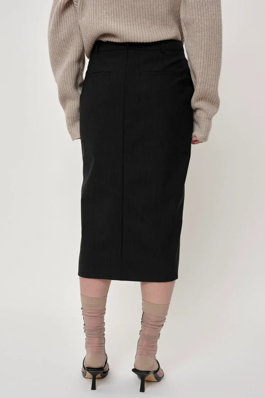 Herskind Mate Skirt – mellemlang nederdel i mørkegrå pinstripe med elegant sideslids. Perfekt pasform og tidløst design.