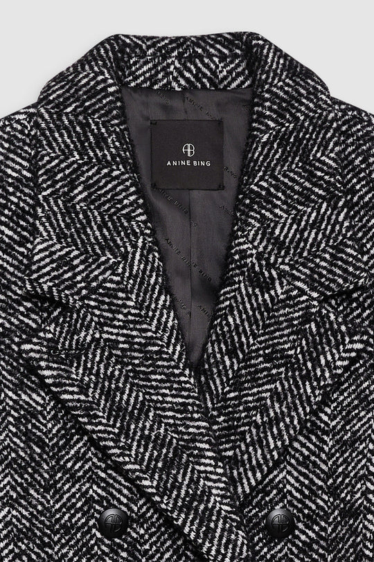 Anine Bing Vienna Blazer i sort og hvid tweed med herringbone-mønster. Cropped snit, dobbeltradet lukning og sofistikerede detaljer for et elegant look.