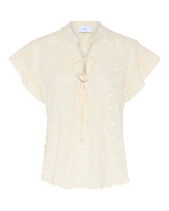 La Rouge Britt Blouse i let bomuld med 3D-blomster, flæseærmer og V-udskæring. Feminin og luftig sommerbluse i creme.