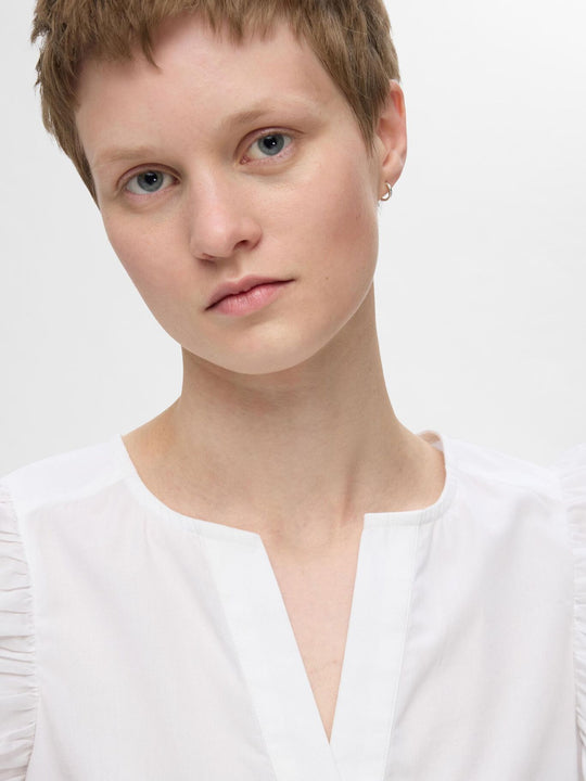 Selected Femme Blair-Ida top i hvid økologisk bomuld med flæsekanter, V-hals og regular fit. Feminin, åndbar og del af et matchende sæt. 