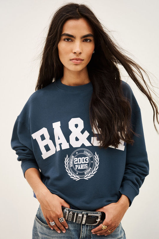 Benjamin sweatshirt i bleu med løs pasform, kort længde og college-inspireret logo. Lavet i økologisk bomuld med stræk. 