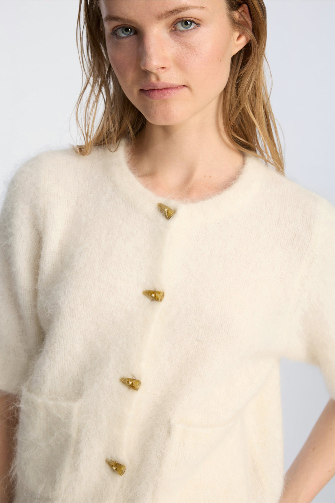 Munthe Locca Knit i ivory – kort strikcardigan med korte ærmer, knaplukning og forlommer med børstet finish.

