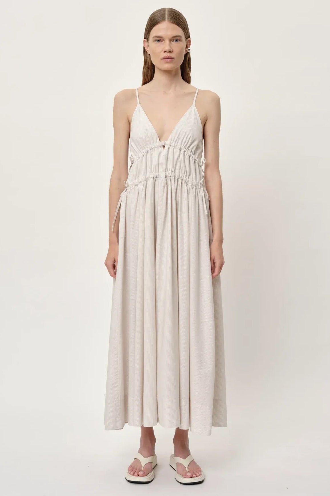 Herskind Miranda Dress i creme pinstripe – lang V-hals kjole med horisontale cutlines og justerbar snøre. 