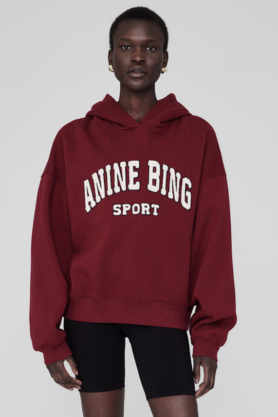 Anine Bing Alec Hoodie Sport i cabernet rød. Chenille patch i ivori og sort broderi. Let oversized pasform med kortere længde for en afslappet, sporty stil.