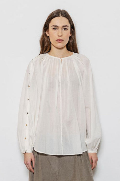 Project AJ117 Hester Bluse i White – feminin skjorte med gathered hals, raglanærmer, dekorative knapper og afrundet kant, fremstillet i 100% økologisk bomuldsvoile.
