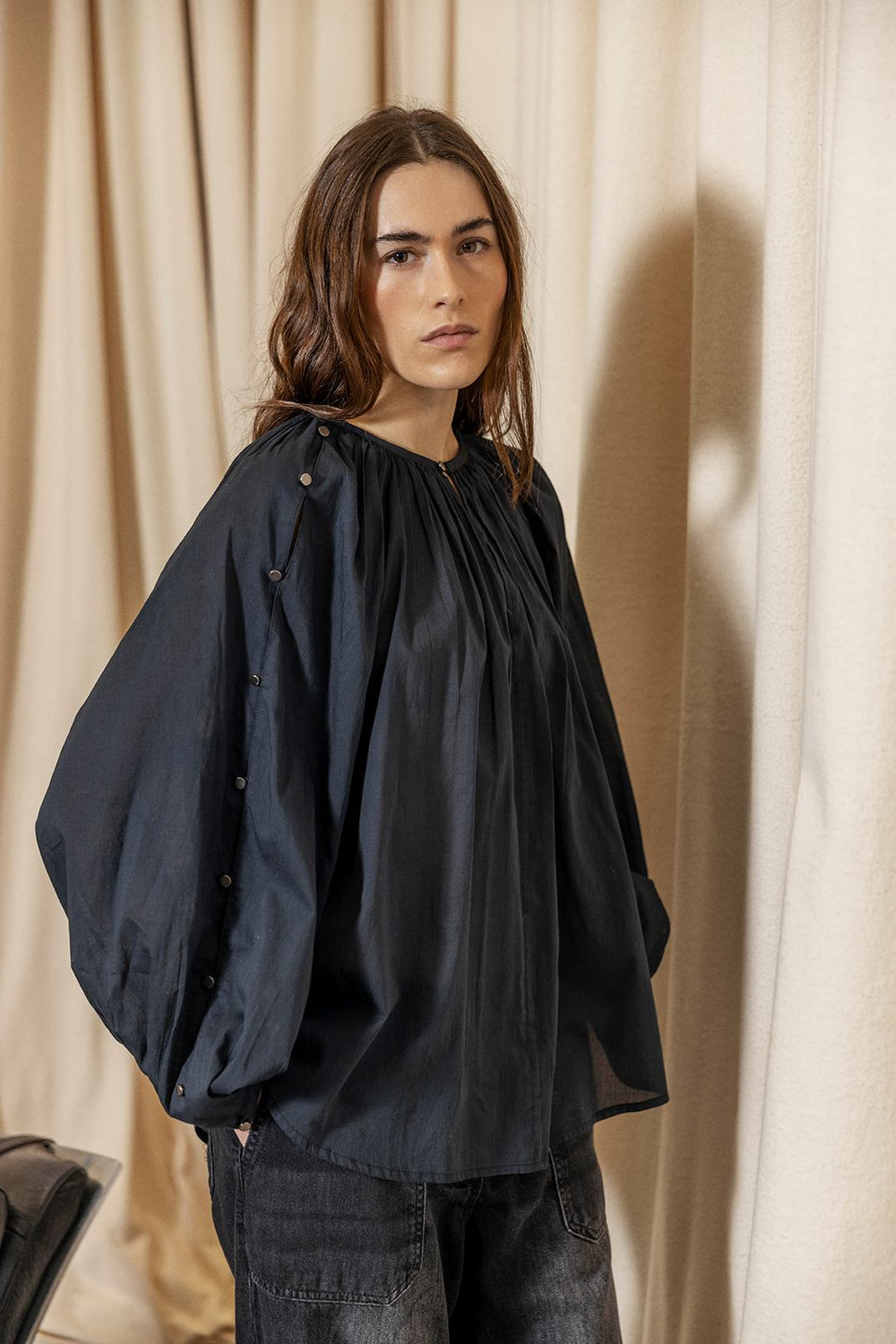 Project AJ117 Hester Bluse i Black – feminin skjorte med gathered hals, raglanærmer, dekorative knapper og afrundet kant, fremstillet i 100% økologisk bomuldsvoile.
