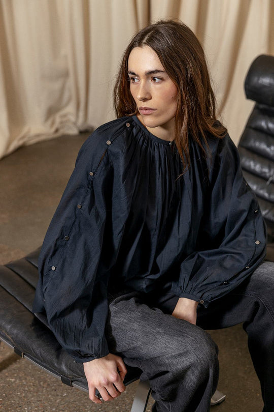 Project AJ117 Hester Bluse i Black – feminin skjorte med gathered hals, raglanærmer, dekorative knapper og afrundet kant, fremstillet i 100% økologisk bomuldsvoile.
