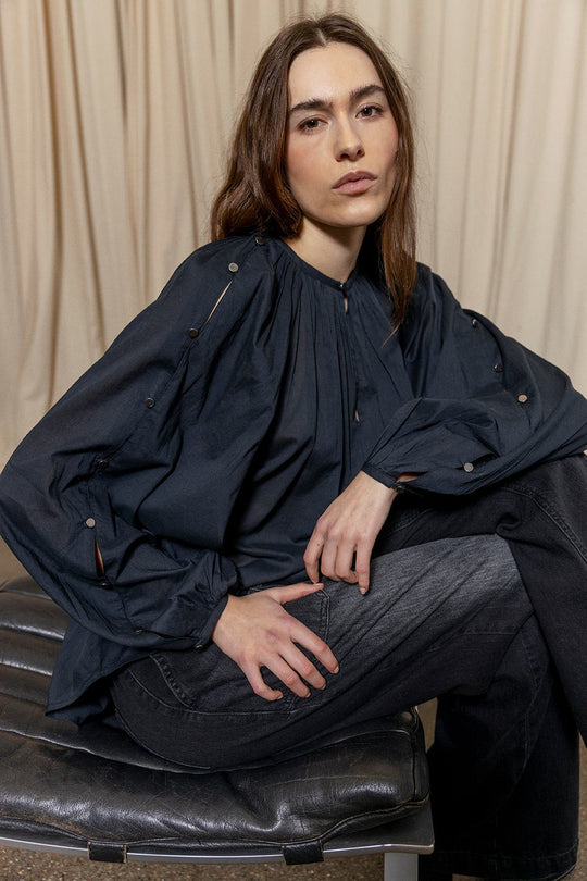 Project AJ117 Hester Bluse i Black – feminin skjorte med gathered hals, raglanærmer, dekorative knapper og afrundet kant, fremstillet i 100% økologisk bomuldsvoile.
