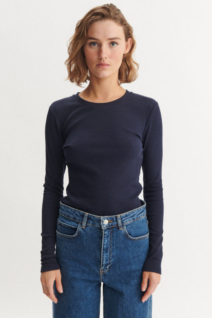 Basic Apparel Ludmilla LS Tee i sky captain – tætsiddende bluse i økologisk bomuld med ribstruktur, lange ærmer og afrundet hals.
