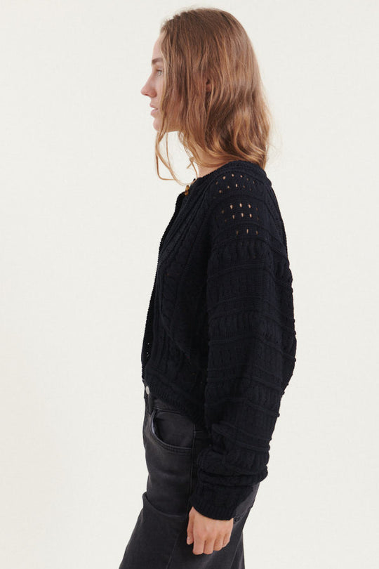 Basic Apparel Winie Cardigan i sort med strikket mønster, stolpelukning og rund hals i økologisk bomuld.
