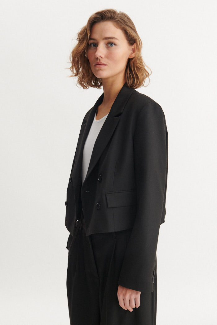 Basic Apparel Radi Short Jakke i sort – let, dobbeltradet jakke i genanvendt polyester med reverskrave og løs pasform.
