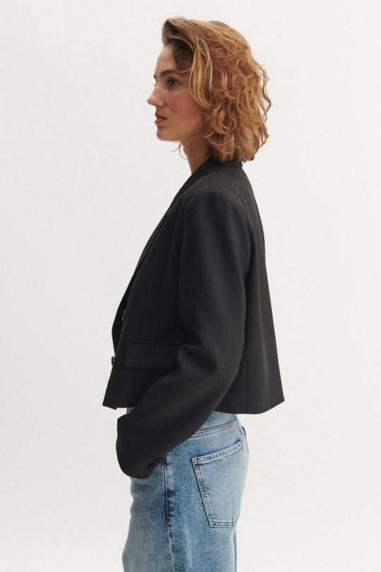 Basic Apparel Radi Short Jakke i sort – let, dobbeltradet jakke i genanvendt polyester med reverskrave og løs pasform.
