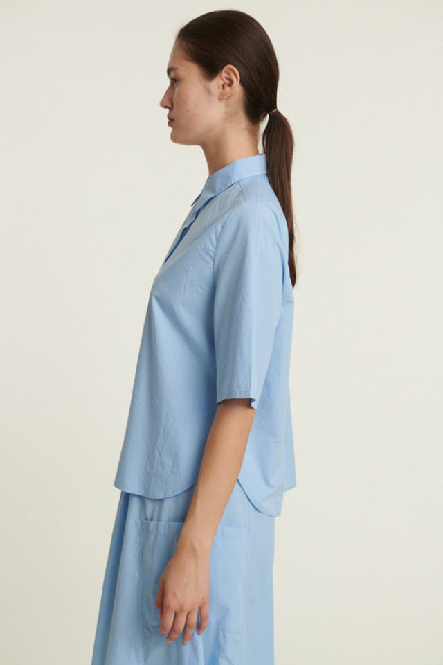 Basic Apparel Silje SS Shirt i frozen fjord med kortærmer, knaplukning, buet kant og løst fit i økologisk bomuld.
