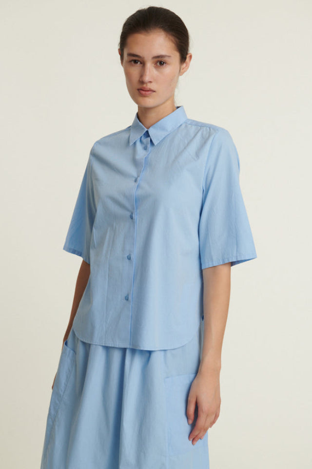 Basic Apparel Silje SS Shirt i frozen fjord med kortærmer, knaplukning, buet kant og løst fit i økologisk bomuld.
