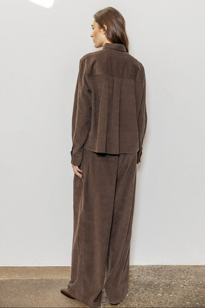Project AJ117 Tailor Bukser i Coffee – brede bukser i blød baby-corduroy med for-pliéer, stiklommer og klassisk lynlås- og knaplukning. Fremstillet i 100% økologisk bomuld.
